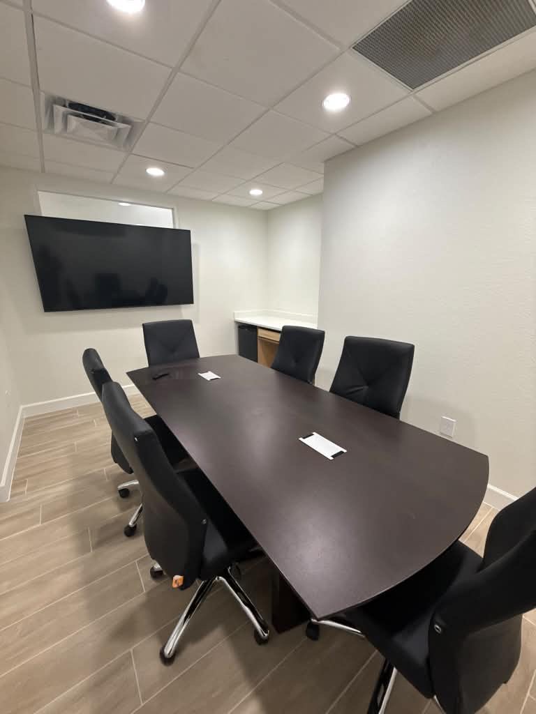 Remodeled office conference room with a wall-mounted TV, dark conference table and wood-look tile flooring